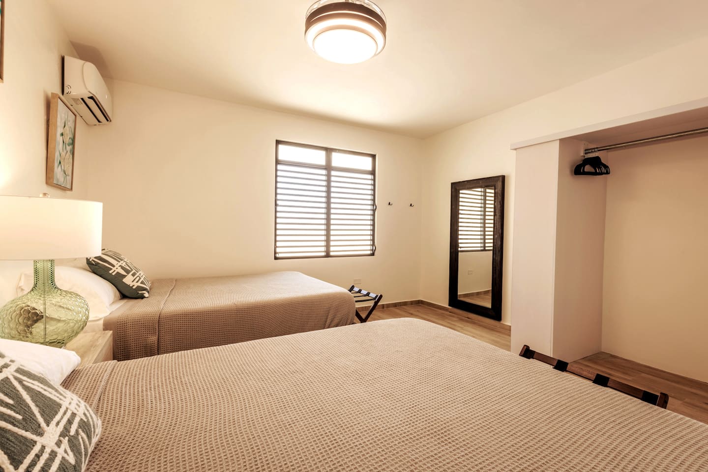 Bedroom with two queen beds in neutral waffle-weave linens, a full-length mirror, open closet and split-unit AC